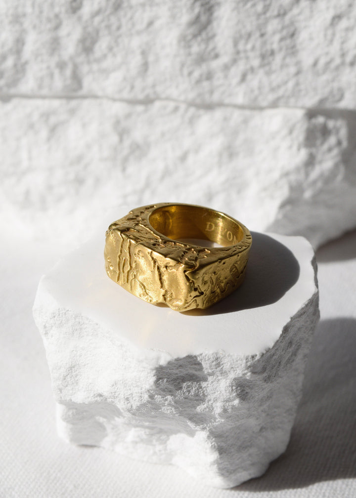 Cracked gold ring by Divon Jewelry, 18K gold-plated, showcased on a white textured stone for a minimalist aesthetic.