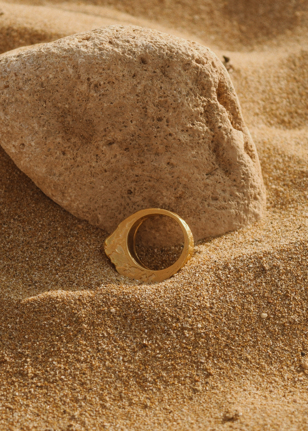 A DIVON Cracked Ring sits on top of a rock in the sand.