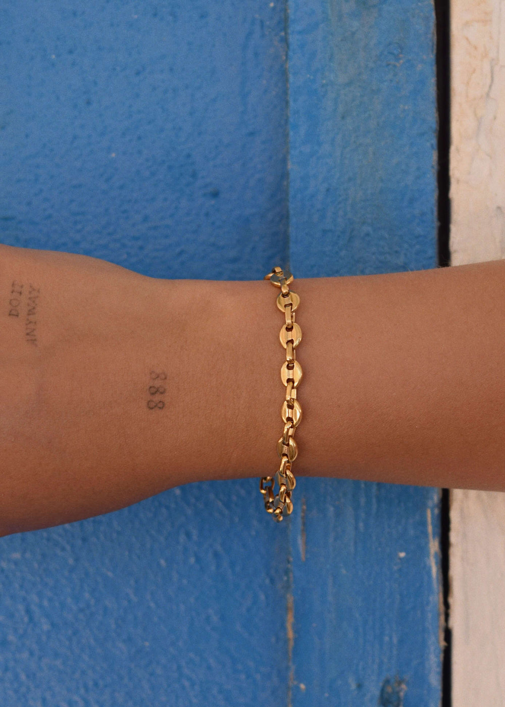 Layered gold bracelets including DIVON Marina 6mm – styled stack on blue summer background