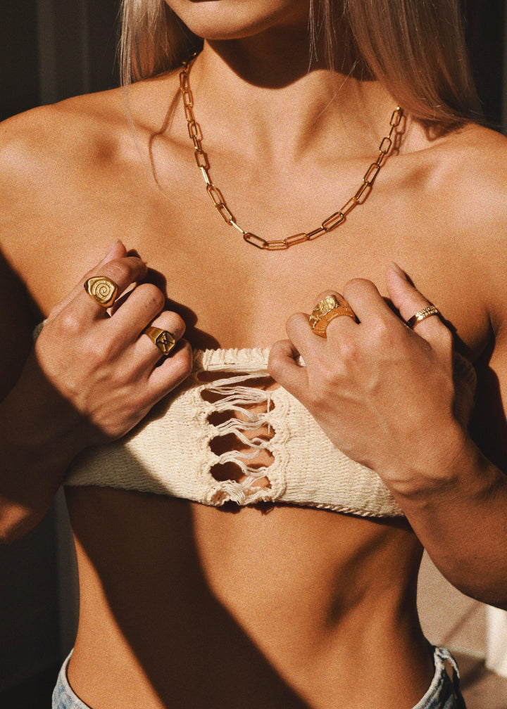 Model wearing multiple gold rings, including the cracked gold ring by Divon Jewelry, styled with a gold chain necklace and a textured top.