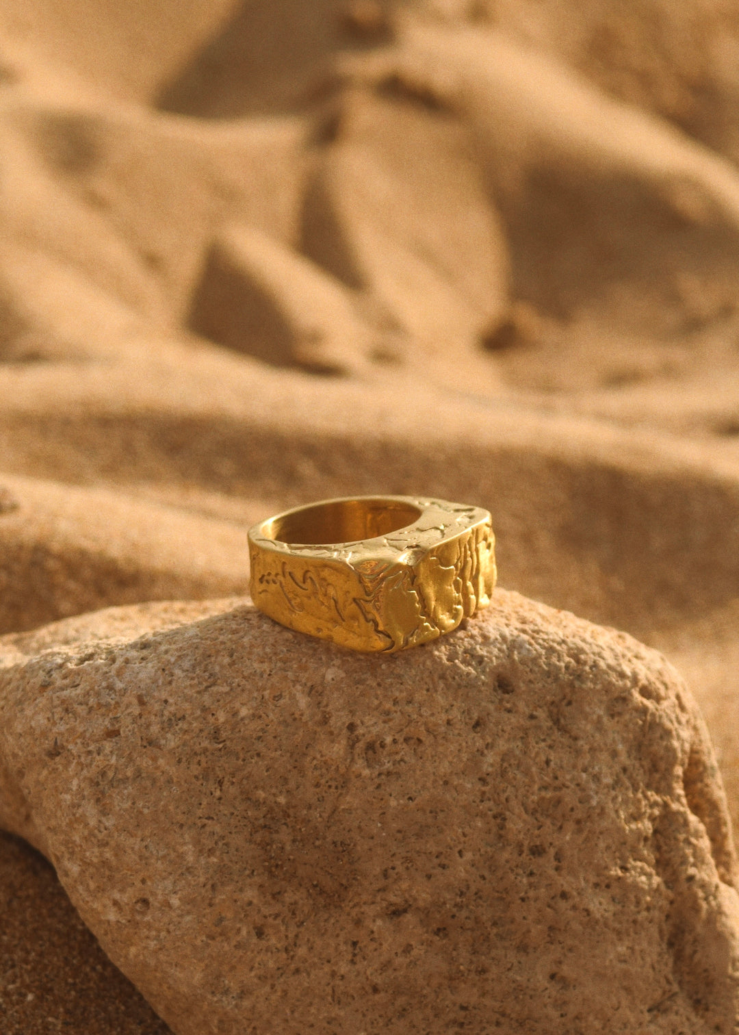 Cracked gold ring by Divon Jewelry, 18K gold-plated, placed on a natural stone in a sandy desert setting for a rustic look.