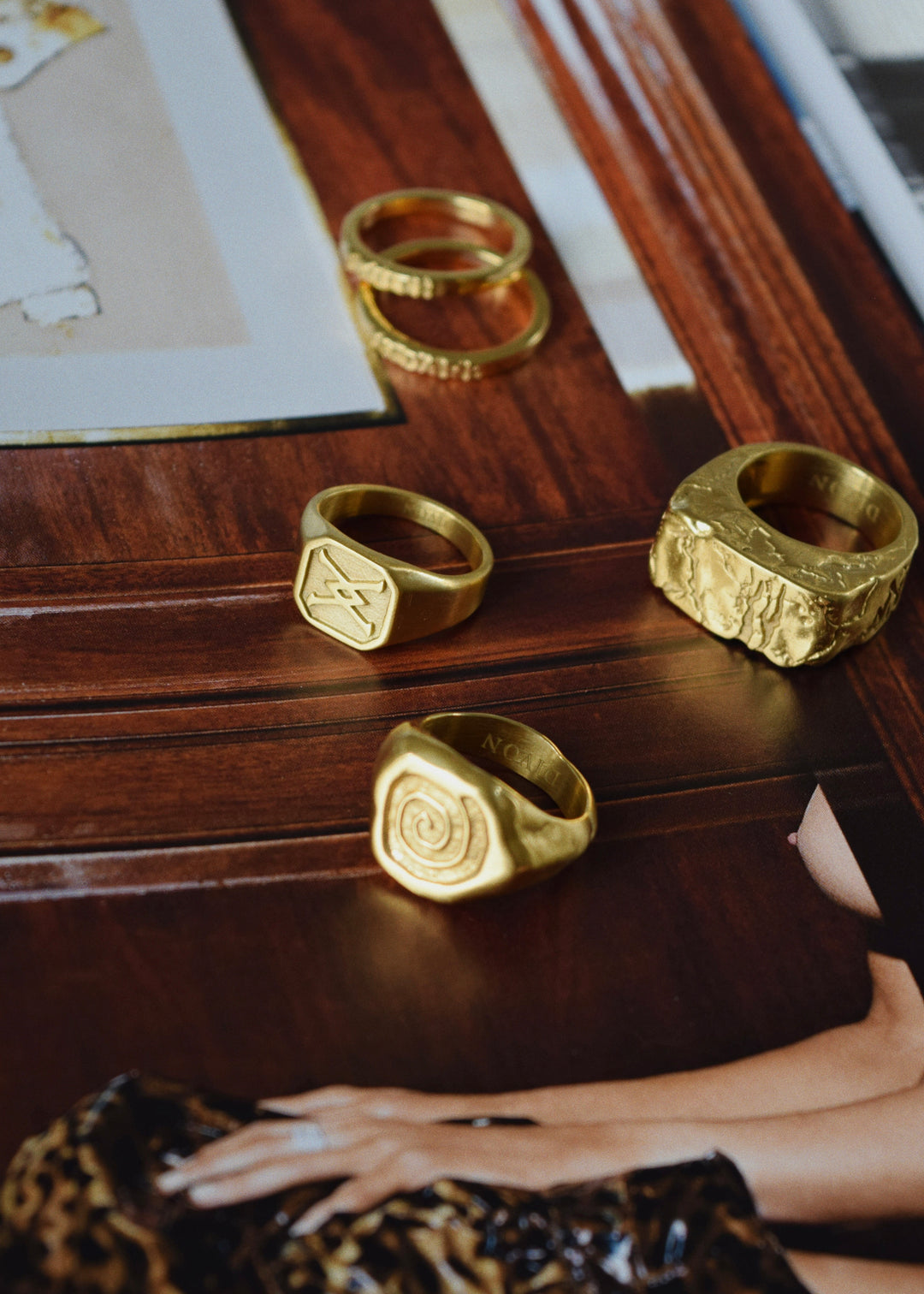 Collection of gold rings, including the handcrafted cracked gold ring by Divon Jewelry, arranged on a wooden surface with magazines.