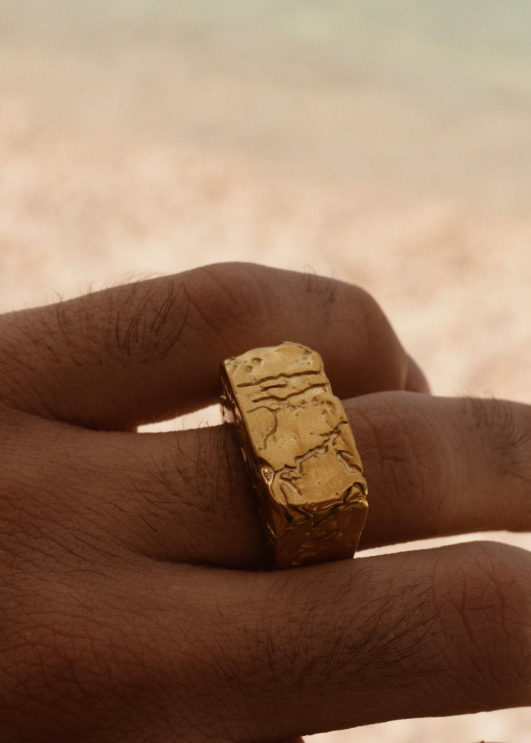 A person wearing a gold ring on a beach.