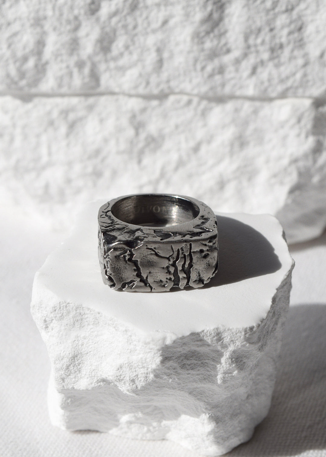 A silver DIVON ring sitting on top of a rock.